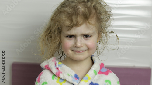 Little girl with wet hair in bathrobe making faces. Smiles after bathing