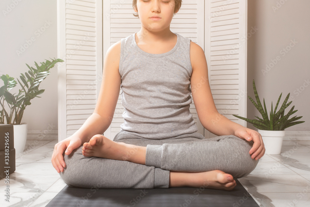 lotus position. meditation. pranayama. children yoga at home. boy wearing gray clothes sitting on a gray yoga mat in a white light room lotus position. meditation. pranayama. children yoga at home. boy wearing gray clothes sitting on a gray yoga mat in a white light room