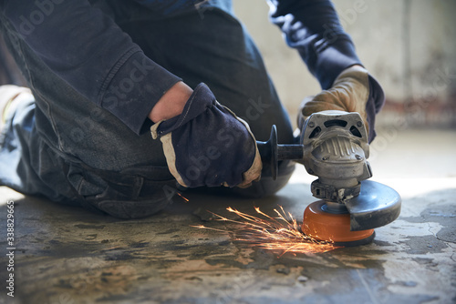 A man in gloves and protective knee pads on the legs grinds the floor with a grinder photo