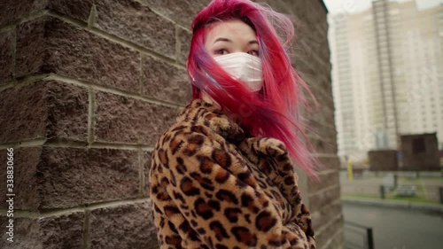 Concept: urban healthcare during pollution pandemic. Beautiful young asian girl with colored hair in medical mask wearing grunge fashion clothing walk street. 100fps in 25fps slow motion.