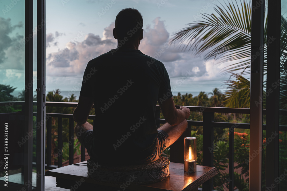 A man sits on a balcony in lotus position at dawn and meditates