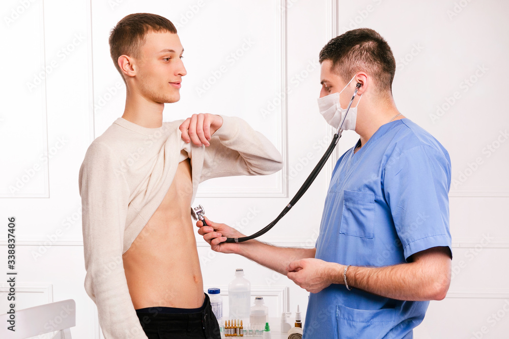 Cheking lungs for pneomonia, coronavirus and covid19 infection. Male doctor with stethoscope listening young boy to lung and heart sound. Healthcare. Family doctor. Cheking lungs for pneomonia, coronavirus and covid19 infection. Male doctor with stethoscope listening young boy to lung and heart sound. Healthcare. Family doctor.