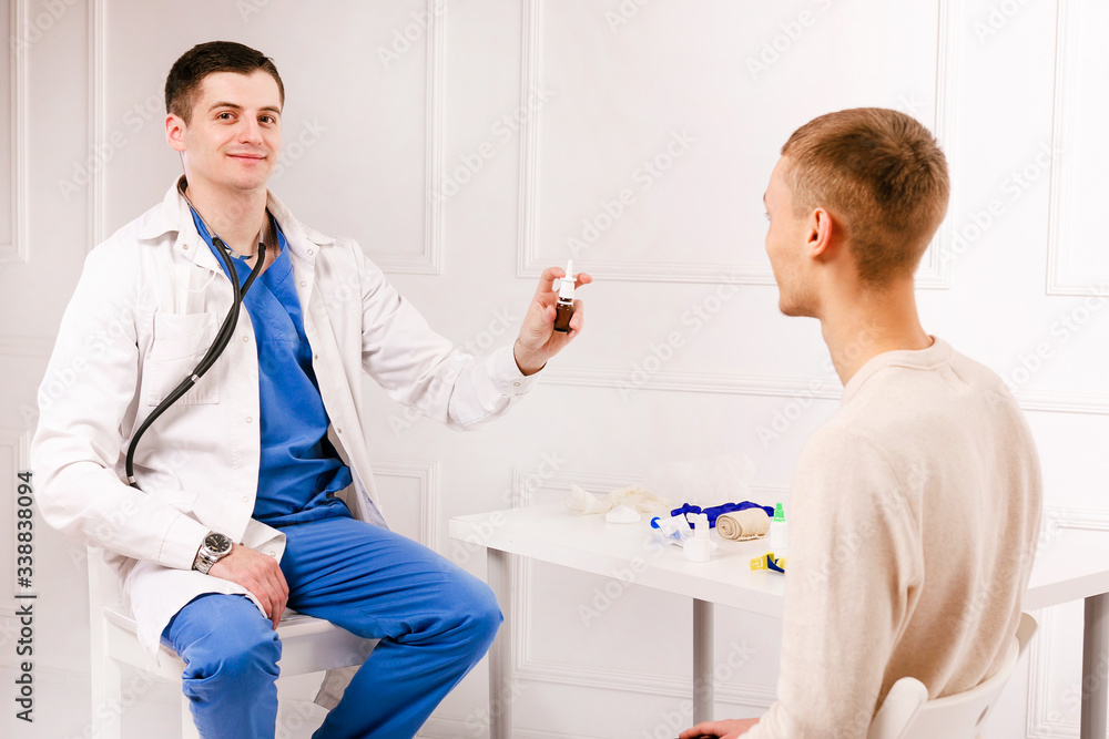 Obraz premium Male handsome doctor shoving a nose drops to young male boy patient. Protection from virus covid19, coronavurus. Concept of healhtcare.