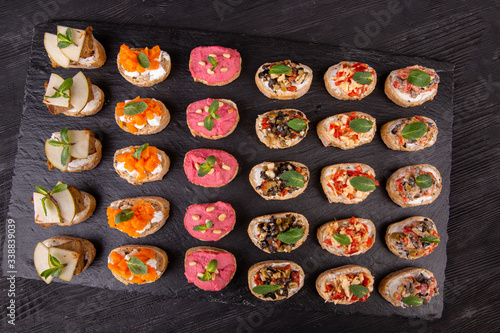 Assorty canape of toast with fish, meat and vegetables on a black background