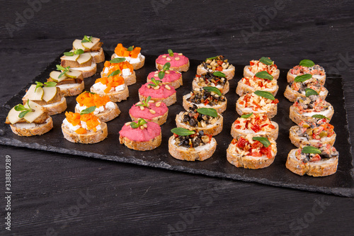 Assorty canape of toast with fish, meat and vegetables on a black background