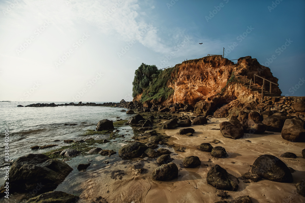 Ocean, sandy beach with large boulders, rock and flying bird. Sri Lanka.