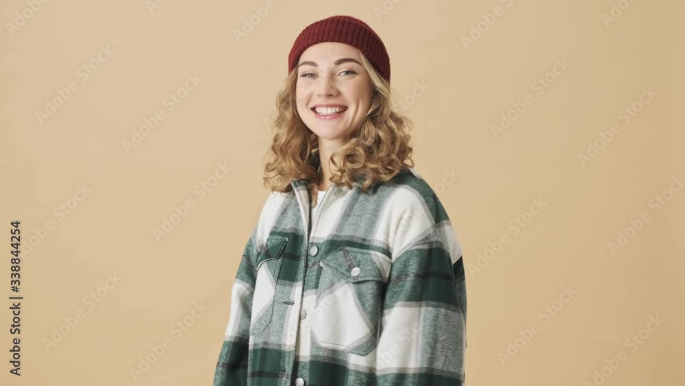 Happy pretty woman in knit hat and shirt posing and looking at the camera over beige background Happy pretty woman in knit hat and shirt posing and looking at the camera over beige background