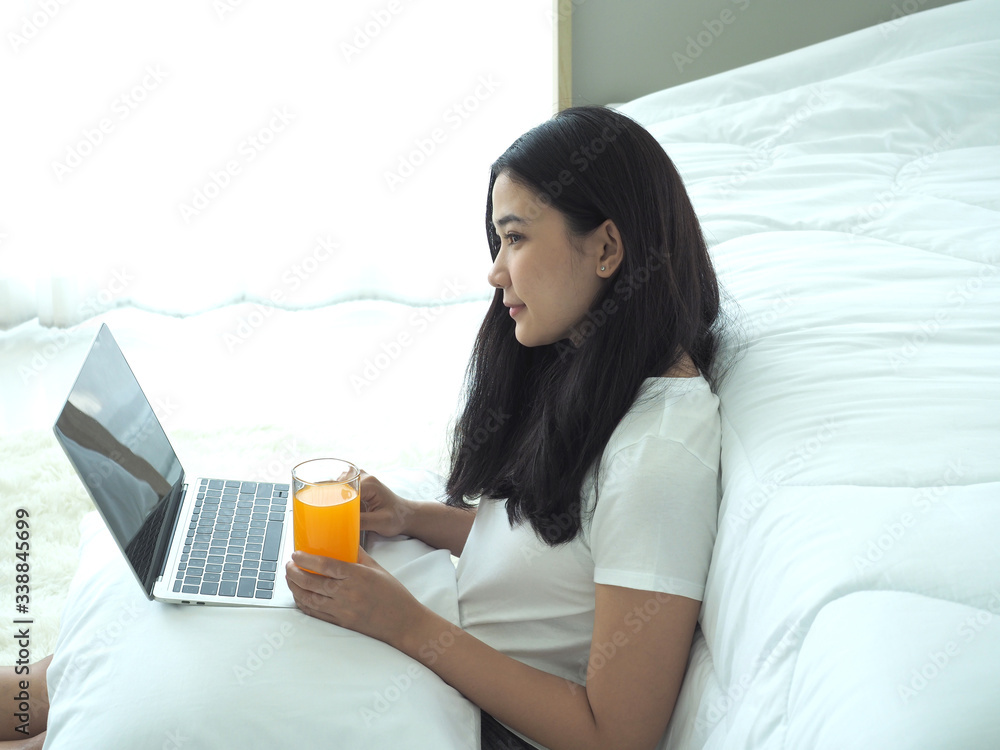 Young asian business woman is using laptop for work from home in her bedroom.She have glass of orange juice.Concept business and coronavirus covid19. Young asian business woman is using laptop for work from home in her bedroom.She have glass of orange juice.Concept business and coronavirus covid19.