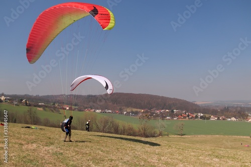 Two paragliders grow handling in a meadow with blue sky on the spring 