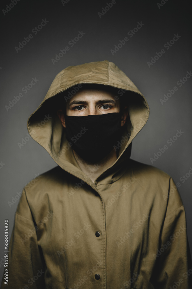 young skinny man wearing a yellow hooded jacket and black face mask with an aggressive serious look
