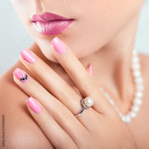 Nail art and design. Beautiful woman wearing make-up and pearl jewellery showing pink manicure with gems.