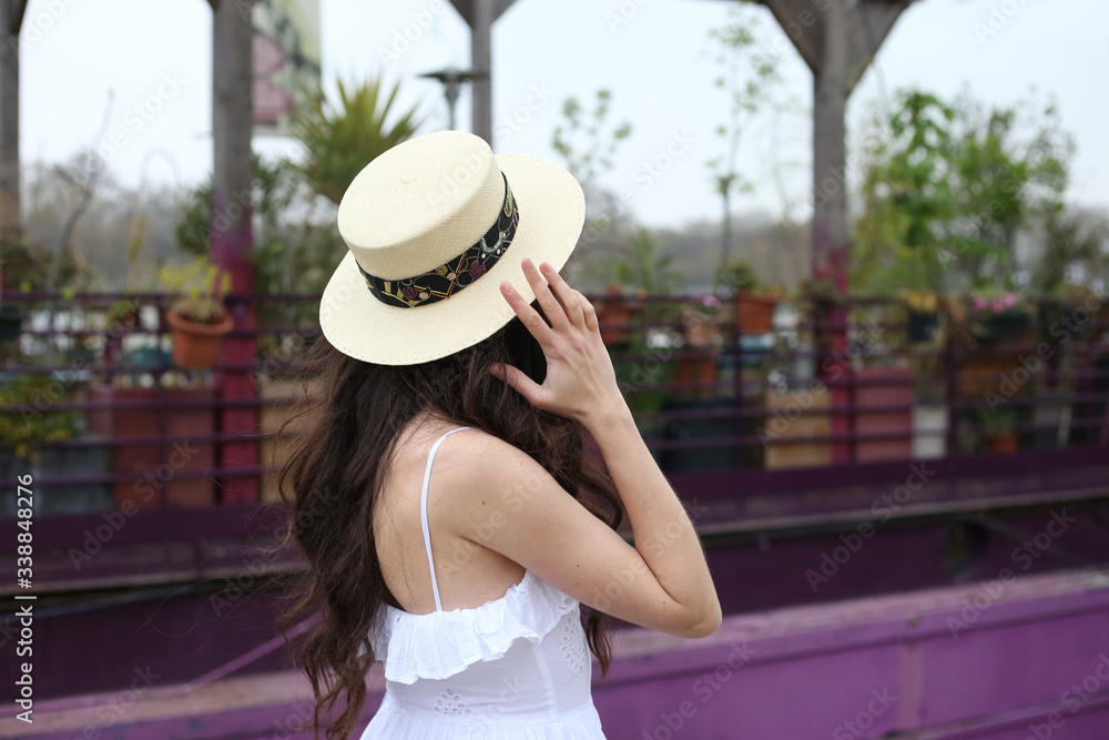 Faceless brunette girl in straw hat and white dress stands alone near purple boat in Paris