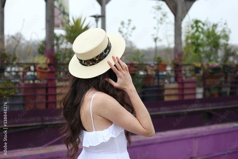 Fototapeta premium Faceless brunette girl in straw hat and white dress stands alone near purple boat in Paris
