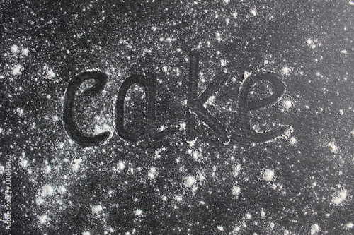 Quadro su tela the word cake on a gray stone black background sprinkled with flour or powdered
