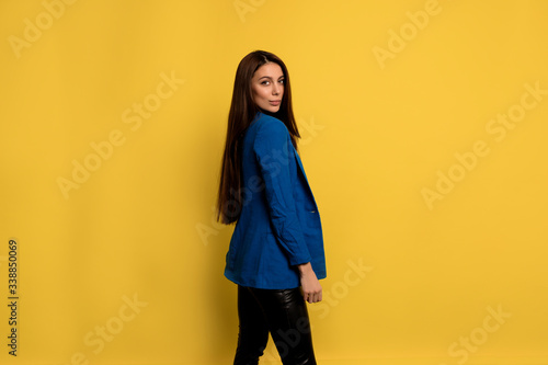 Attractive stylish woman with long dark hair wearing blue jacket posing over isolated background with charming smile © PhotoBook