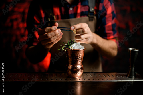 Close-up Barman's hand decorates with spikelet metal glass using tweezers