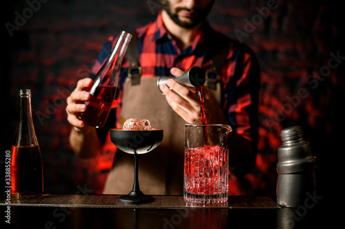 bartender pours red liquid from jigger into mixing cup
