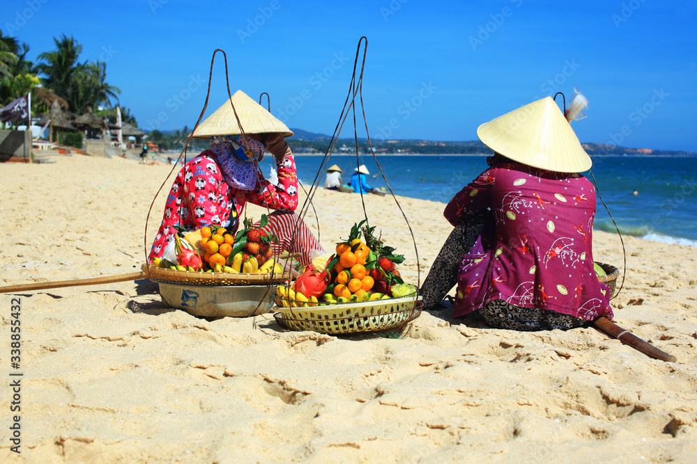 wietnamskie kobiety w tradycyjnych kapeluszach siedzące na plaży - obrazy, fototapety, plakaty 