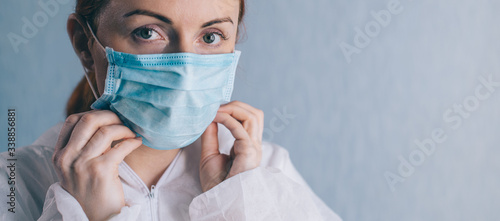 Coronavirus epidemic. A female doctor puts on a face mask and looks at the camera. Close-up. © MZaitsev