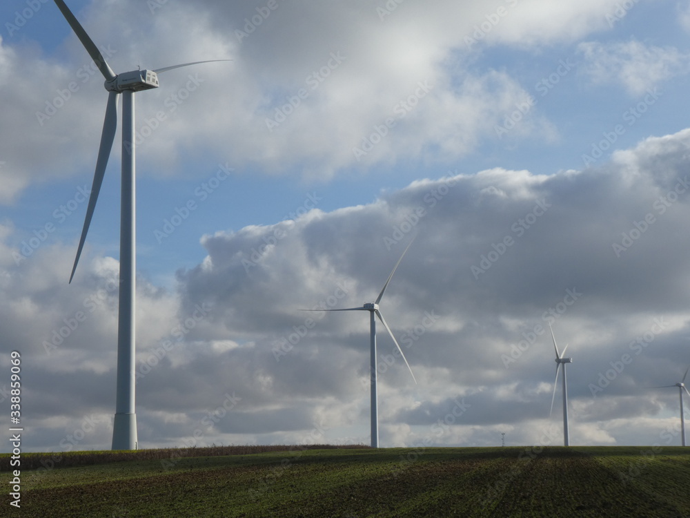 Row of four wind turbines with cottony clouds in a blue sky