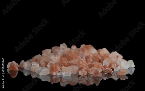 Crystals of pink Himalayan salt on a black mirror surface. Selective focus.
