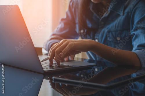 Casual business woman hands holding electronic or stylus pencil and typing on laptop computer keyboard with black digital tablet on the desk at office. Online working concept. Flare light.