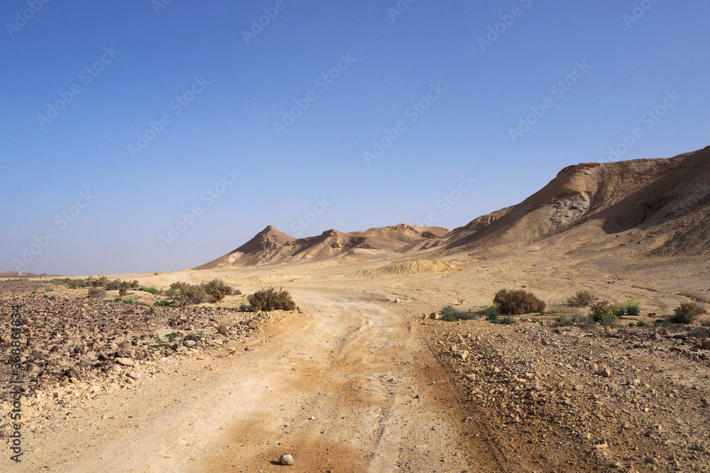 The desert landscape with the yellow sandstone hills, the big ground road, the blue sky with white clouds.