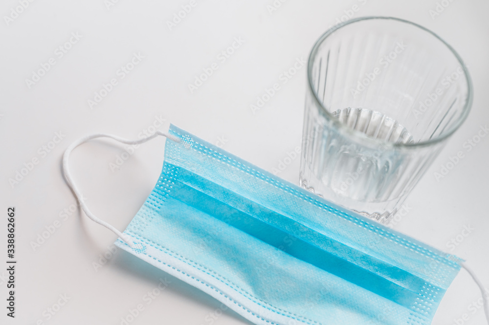 Used protective mask and glass of water on white table. Novel coronavirus 2019 COVID-19 theme. Coronavirus wallpaper on tablet. Coronavirus protection. Used protective mask and glass of water on white table. Novel coronavirus 2019 COVID-19 theme. Coronavirus wallpaper on tablet. Coronavirus protection.