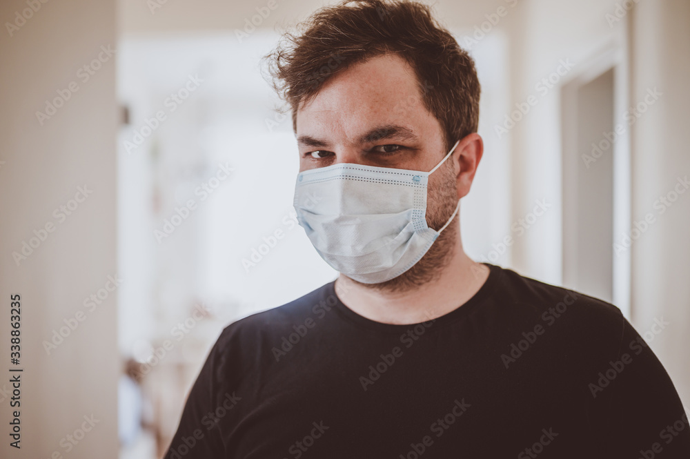 Man in quarantine during coronavirus COVID-19. Man with protective mask stands near window. Novel coronavirus 2019 COVID-19 theme. Quarantine during coronavirus pandemic Man in quarantine during coronavirus COVID-19. Man with protective mask stands near window. Novel coronavirus 2019 COVID-19 theme. Quarantine during coronavirus pandemic