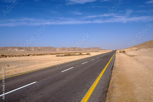 The desert landscape with the far yellow sandstone hills, the big empty black asphalt road, the blue sky with white clouds. © Anna Silanteva