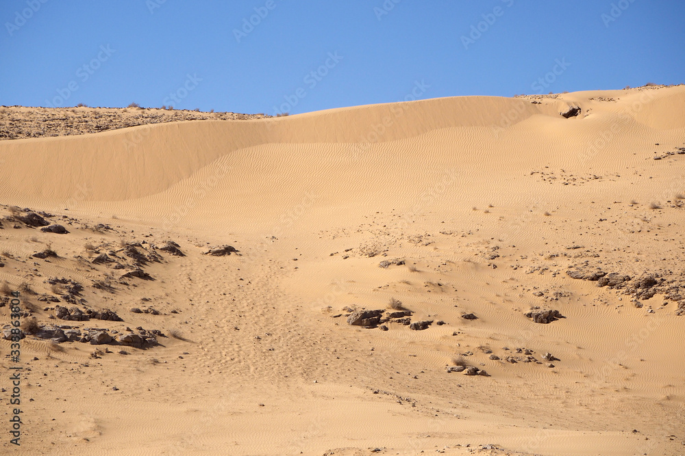 The sand slope with the dark stones on foreground, the big orange sand dune, and the blue sky.