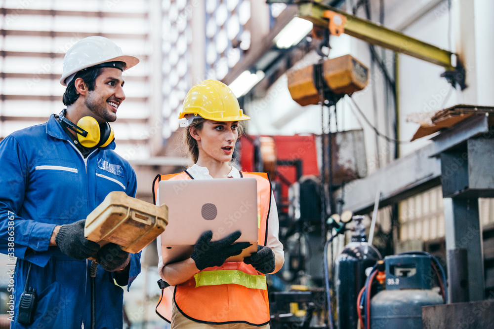 Male and female industrial worker or engineers in hard helmet discuss project while using laptop. Man and woman technician people working in heavy technology invention industry manufacturing factory. Male and female industrial worker or engineers in hard helmet discuss project while using laptop. Man and woman technician people working in heavy technology invention industry manufacturing factory.
