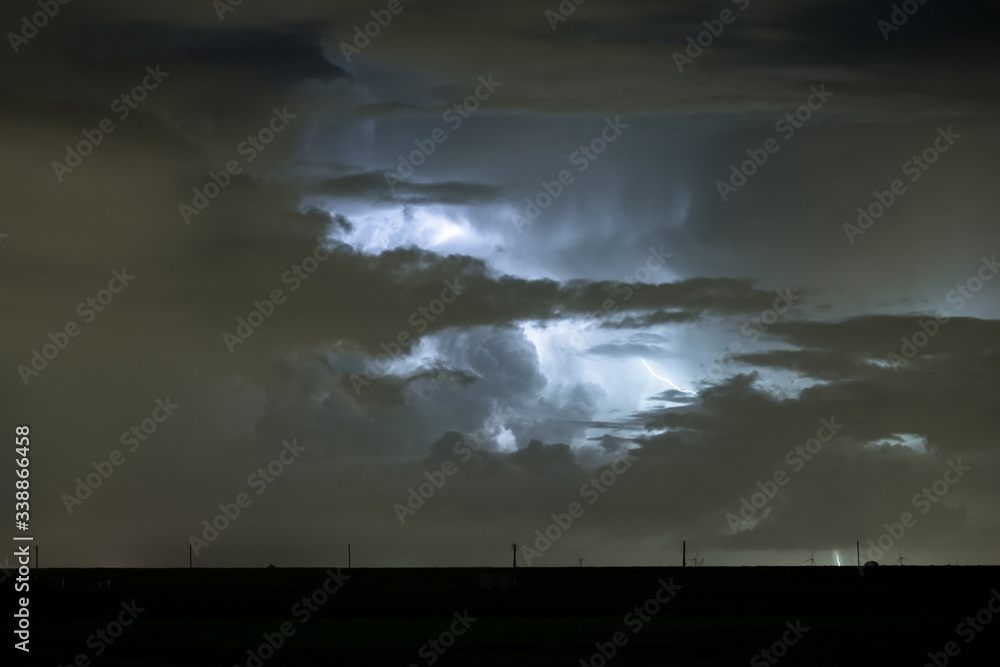 Dramatic landscape image of a cumulonimbus storm cloud illuminated by lightning at night