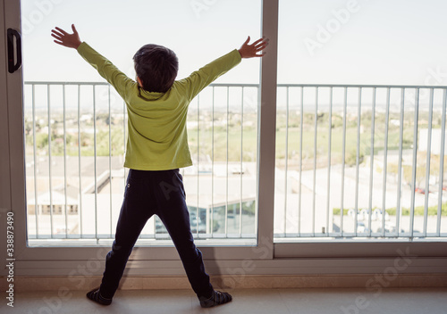 Fototapeta Naklejka Na Ścianę i Meble -  Boy looking outside through the window. Concept of isolation and waiting for the coronavirus lockdown to end
