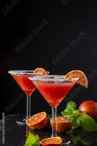 Top view of two blood orange martini glasses, half orange and mint, on black background, vertical, with copy space