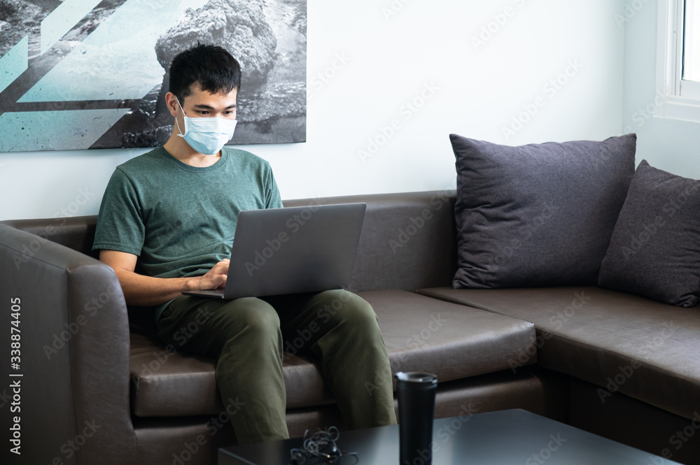 Asian business man wearing face mask working on sofa via laptop at his office.Young male manager using portable computer device in coffee shop.Male hands typing on the keyboard.Work from home. Asian business man wearing face mask working on sofa via laptop at his office.Young male manager using portable computer device in coffee shop.Male hands typing on the keyboard.Work from home.