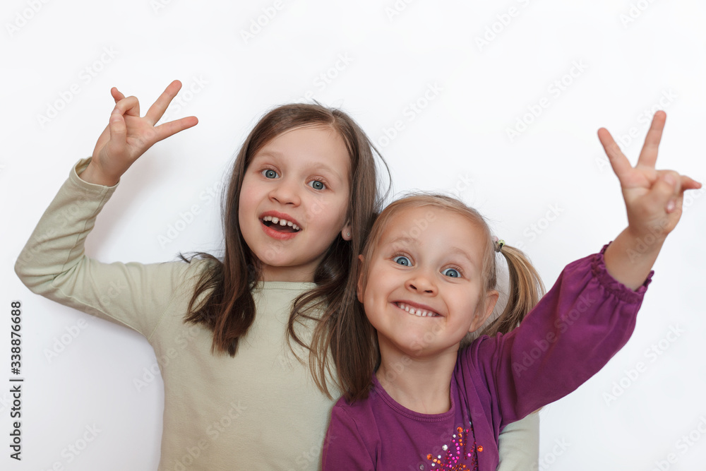 Two little girls on a white gray background looking at the camera and showing a victory sign with their hands Two little girls on a white gray background looking at the camera and showing a victory sign with their hands