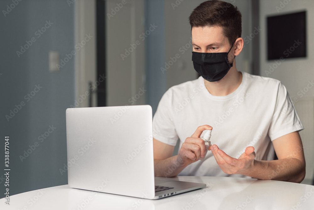 Man working from home during coronavirus quarantine, wearing black protective mask. Working from home. Cleaning her hands with sanitizer gel. Close up photo of sanitizer gel