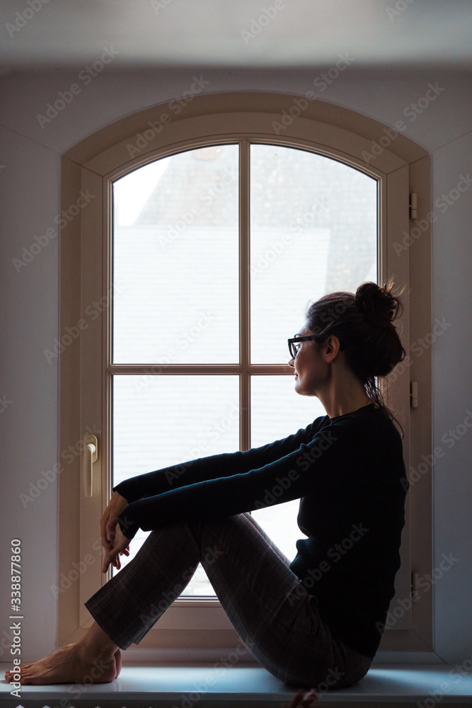 Vertical view of woman worried looking through the window at home. Portrait of concerned mother about coronavirus quarantine in the house. Stay home concept during pandemic covid 19 virus disease.