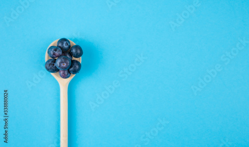 top view of fresh ripe blueberries on wooden spoon on blue background with copy space