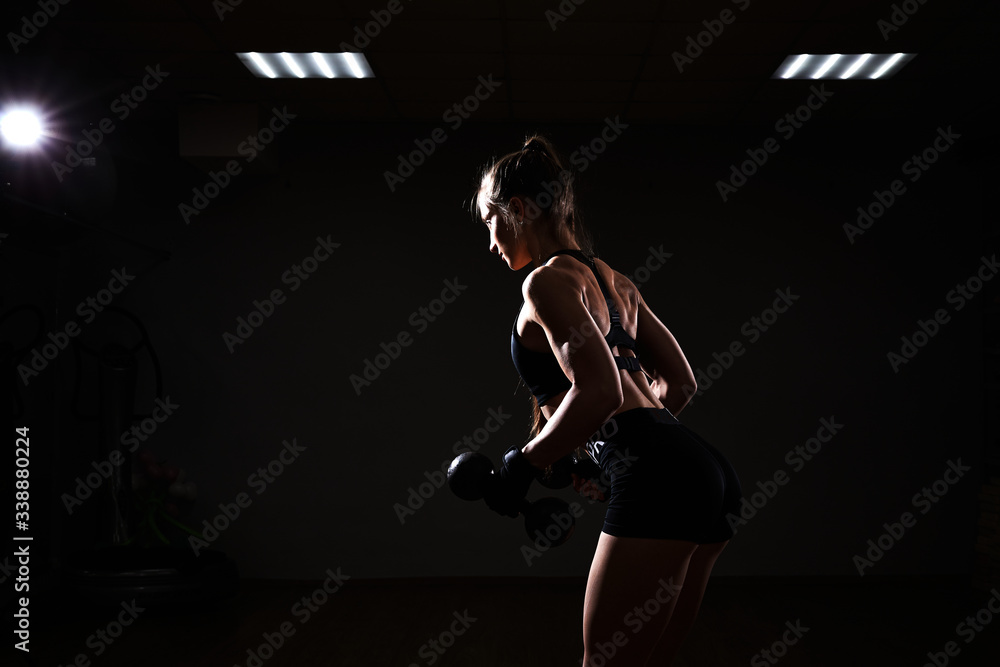 Fitness and sport concept. Brutal athletic woman pumping up muscules with dumbbells on dark background. Fitness and sport concept. Brutal athletic woman pumping up muscules with dumbbells on dark background.