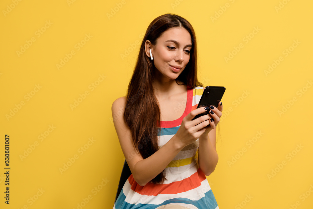 Close-up portrait of attractive dreamy woman isolated on yellow background. Close-up portrait of adorable girl in summer clothes touching earphones during photoshoot.