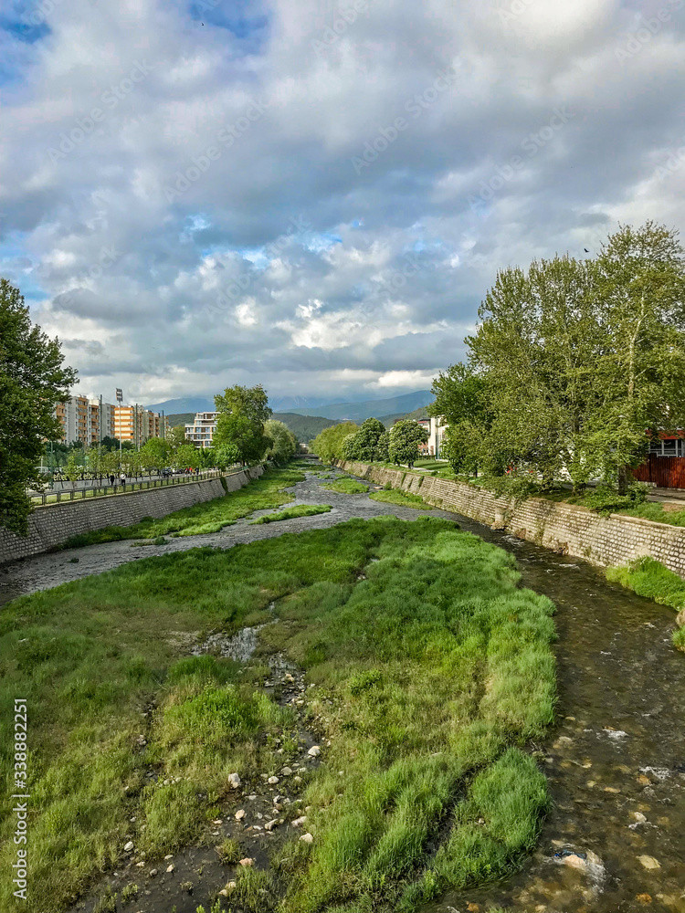 A small river flowing through a town in a dike with fluffy clouds above 