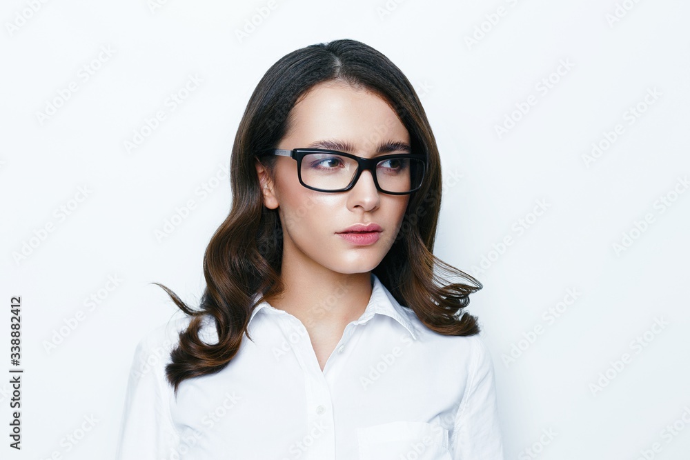 Portrait of young brunette woman with a healthy clean skin. Young beautiful business woman in stylish glasses and white shirt posing in studio. Portrait of young brunette woman with a healthy clean skin. Young beautiful business woman in stylish glasses and white shirt posing in studio.