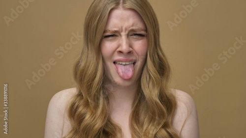 A displeased young half-naked woman with long hair is looking at something disgusting isolated over beige background