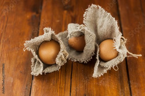 Eggs stand on a burlap that stands on a brown wooden table. Top views with clear space