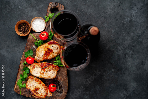 Dinner for two, grilled pork steaks with spices, a bottle of wine and glasses on a stone background with copy space for your text