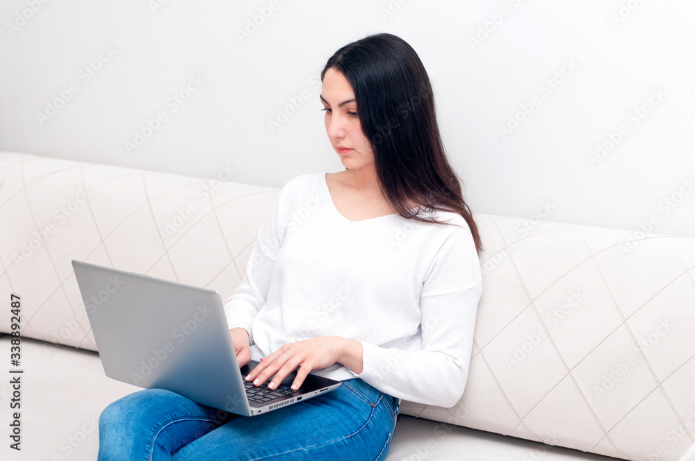 Young caucasian woman sitting on sofa working on laptop. Beautiful girl using notebook, work from home, relaxing on couch. Remote work, telecommuting, quarantine, digital nomad, stay at home concept. Young caucasian woman sitting on sofa working on laptop. Beautiful girl using notebook, work from home, relaxing on couch. Remote work, telecommuting, quarantine, digital nomad, stay at home concept.