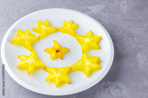 Carambola on a white plate. Sliced carambola on a gray background. Slices of star fruit. Trendy food. Copy space