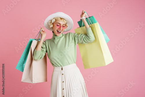 Spring shopping concept: happy smiling fashionable woman wearing trendy clothes posing with colorful paper bags. Pink background. Copy, empty space for text
